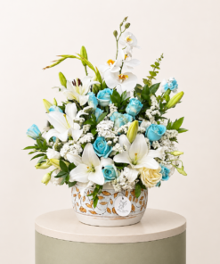 Luxury floral arrangement featuring white lilies, white orchids, blue roses, and fresh greenery in a decorative vase.