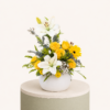 Luxury flower arrangement featuring yellow roses, white lilies, gerbera flowers, and fresh greenery in a white ceramic vase.
