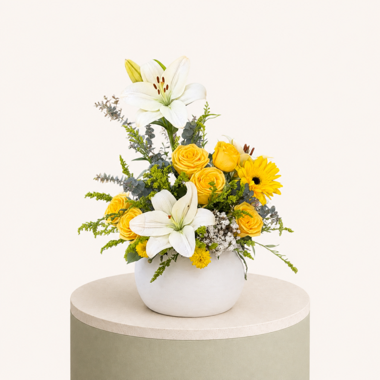 Luxury flower arrangement featuring yellow roses, white lilies, gerbera flowers, and fresh greenery in a white ceramic vase.