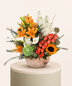 Luxury floral arrangement featuring orange lilies, peach roses, sunflower, white calla lilies, and eucalyptus in a decorative vase.