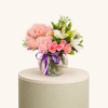 Elegant flower arrangement with pink roses, white lilies, and a soft pink teddy bear in a glass vase by Marino Flowers.