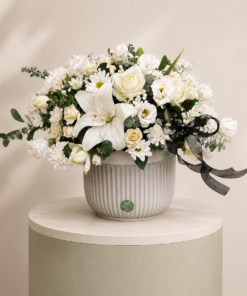 Luxury white floral arrangement with lilies, roses, chrysanthemums, lisianthus, and eucalyptus in an elegant ceramic vase.