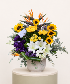 Luxury sunflower and lily arrangement with yellow roses, birds of paradise, and purple lisianthus in a ceramic vase.