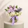 Lavender rose flower arrangement with white freesia, lilies, stock flowers, and greenery in a glass vase.