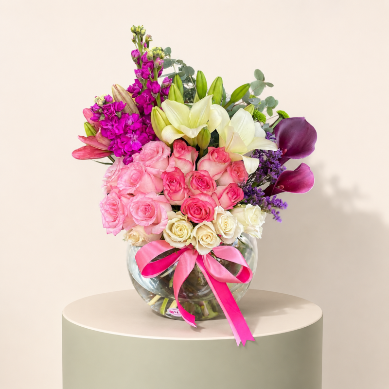 Luxury arrangement of pink roses, white lilies, cream roses, purple calla lilies, stock flowers, and greenery in a glass bowl by Marino Flowers.