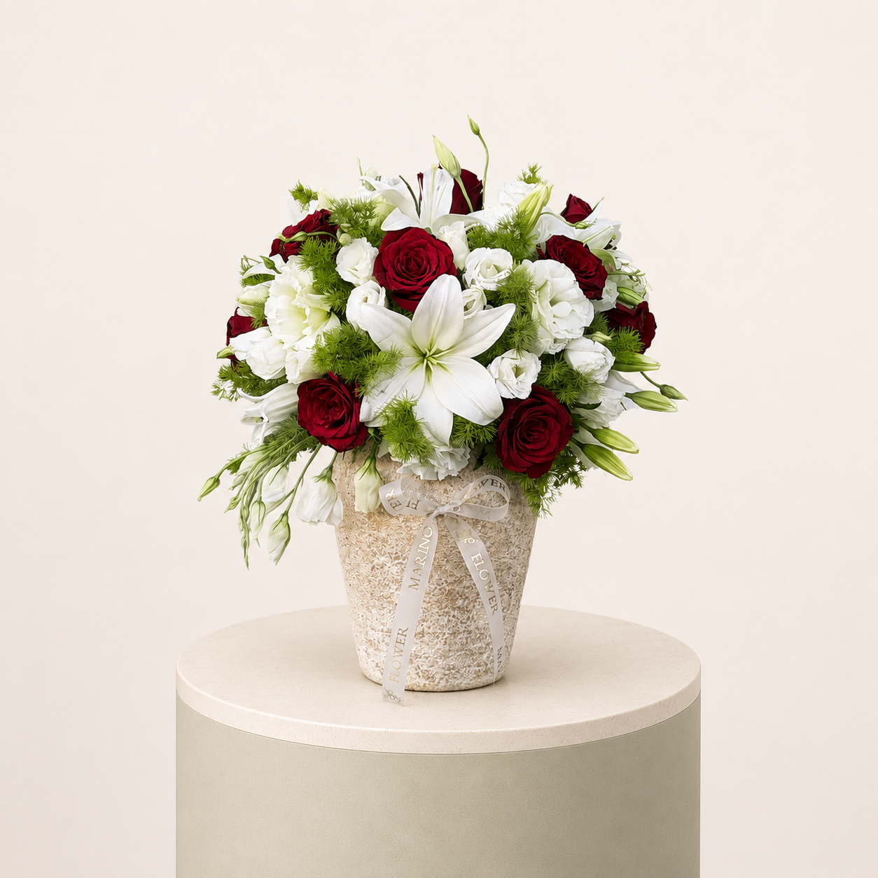 Red roses and white lilies arranged with white flowers and greenery in an elegant cream vase by Marino Flowers