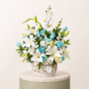 Luxury floral arrangement featuring white lilies, white orchids, blue roses, and fresh greenery in a decorative vase.