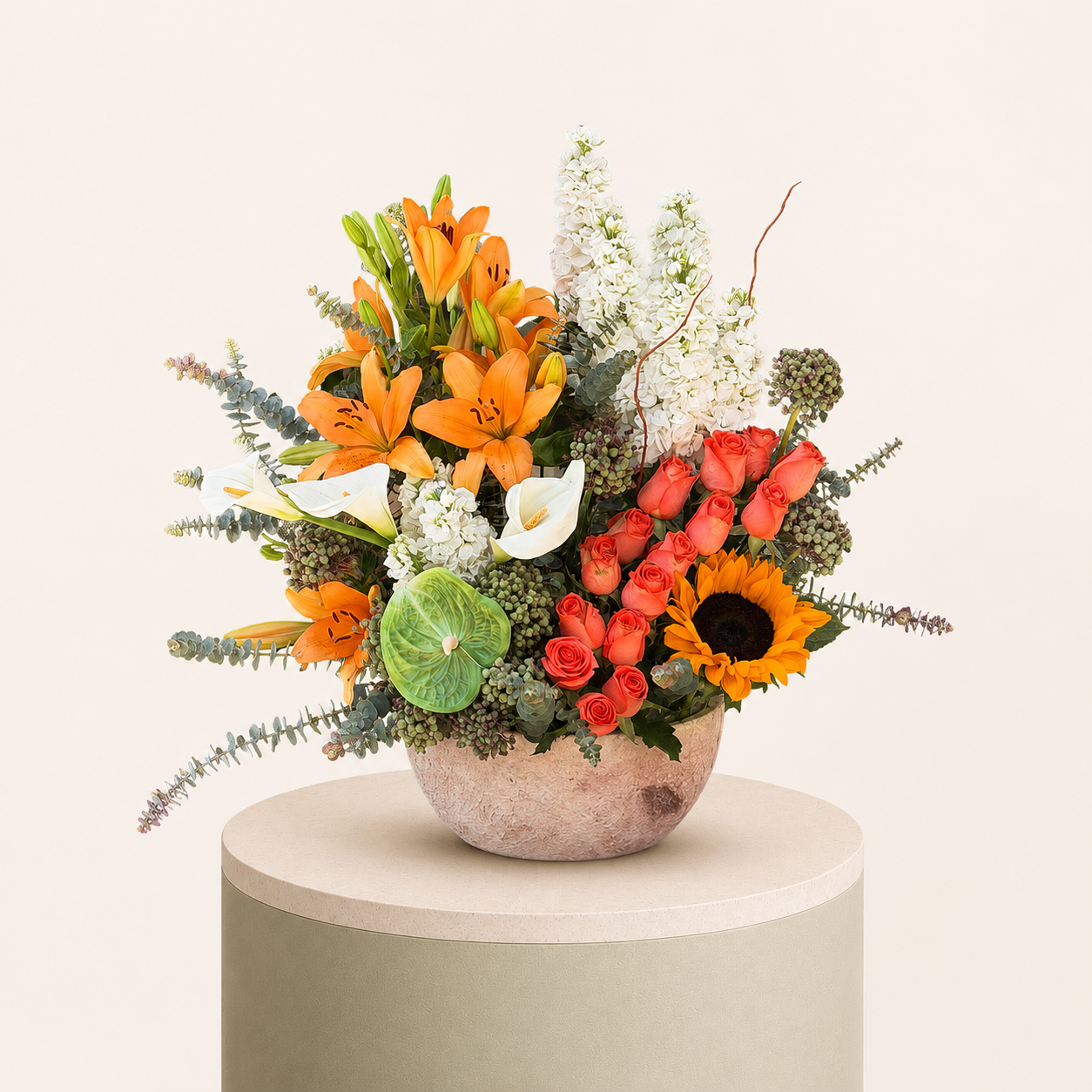 Luxury floral arrangement featuring orange lilies, peach roses, sunflower, white calla lilies, and eucalyptus in a decorative vase.