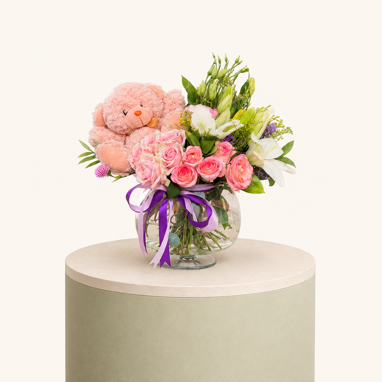 Elegant flower arrangement with pink roses, white lilies, and a soft pink teddy bear in a glass vase by Marino Flowers.