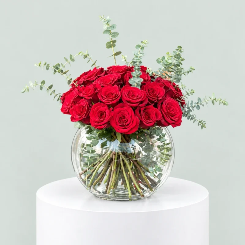 Luxury arrangement of deep red roses and silver-green eucalyptus in a clear round glass fishbowl vase by Marino Flowers.